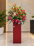 Red gerberas and pink lilies in a FlowerPlus Grandeur standee for grand openings, featuring vibrant tropical floral arrangement.